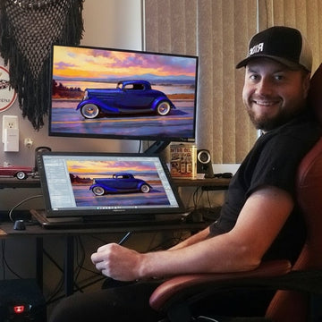 Wes Klee at his digital painting desk, smiling, with a car painting on the screen behind him